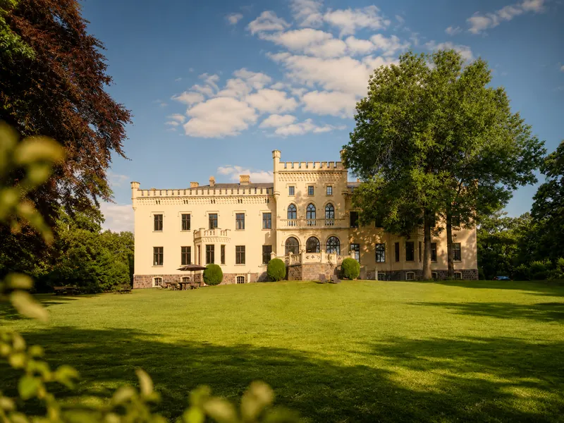 Seeseite von Schloss Reichenow mit großer Wiese und altem Baumbestand